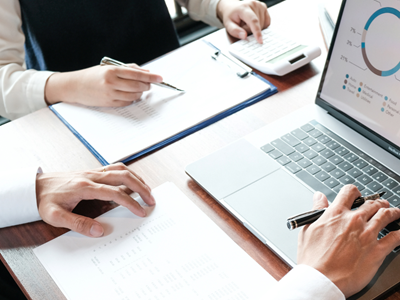 People working at desk on a laptop holding and taking notes